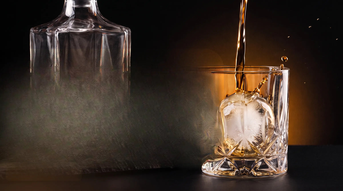 Whisky poured over a large ice sphere beside a crystal decanter
